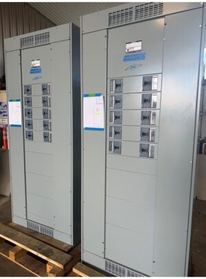 67Panelboard - Siemens 2ea distribution - Coastal Power Systems Two tall gray electrical panels with multiple circuit breakers, vents at top and bottom, placed on wooden pallets in a warehouse.